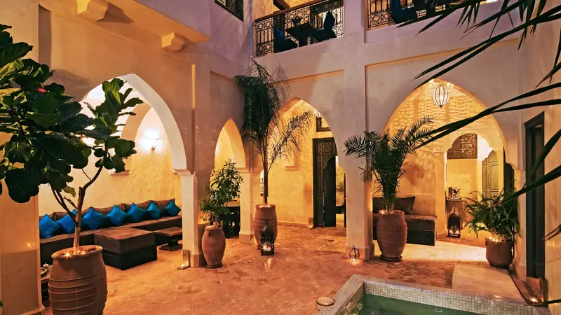 Patio de riad éclairé le soir, avec arcades, banquettes et bassin